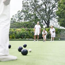 Residents of a retirement village all dressed in white enjoy a game on a local bowling green.