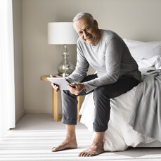 Man sitting on side of bed with tablet in hand
