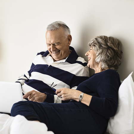 A man and woman are sitting next to each other, looking at a laptop and laughing together.