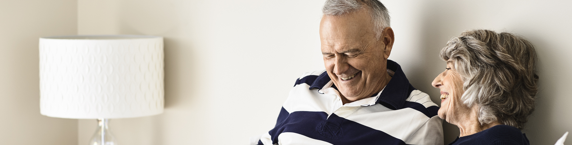 A man and woman are sitting next to each other, looking at a laptop and laughing together.