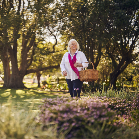 A smiling lady with a basket walking through Closebourne Retirement Village
