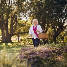 A smiling lady with a basket walking through Closebourne Retirement Village
