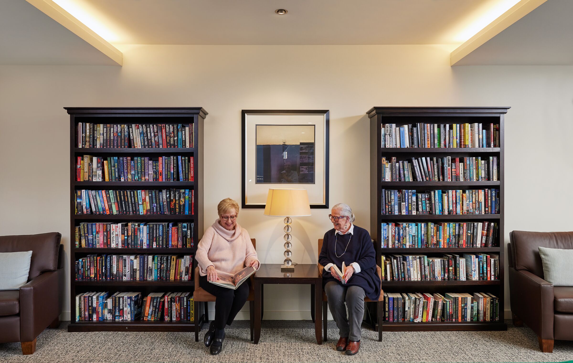 The Brighton on Bay women sitting in library room with well stocked bookcases