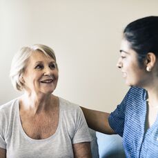 Two women smiling at each other with the younger woman providing care services to the older female.