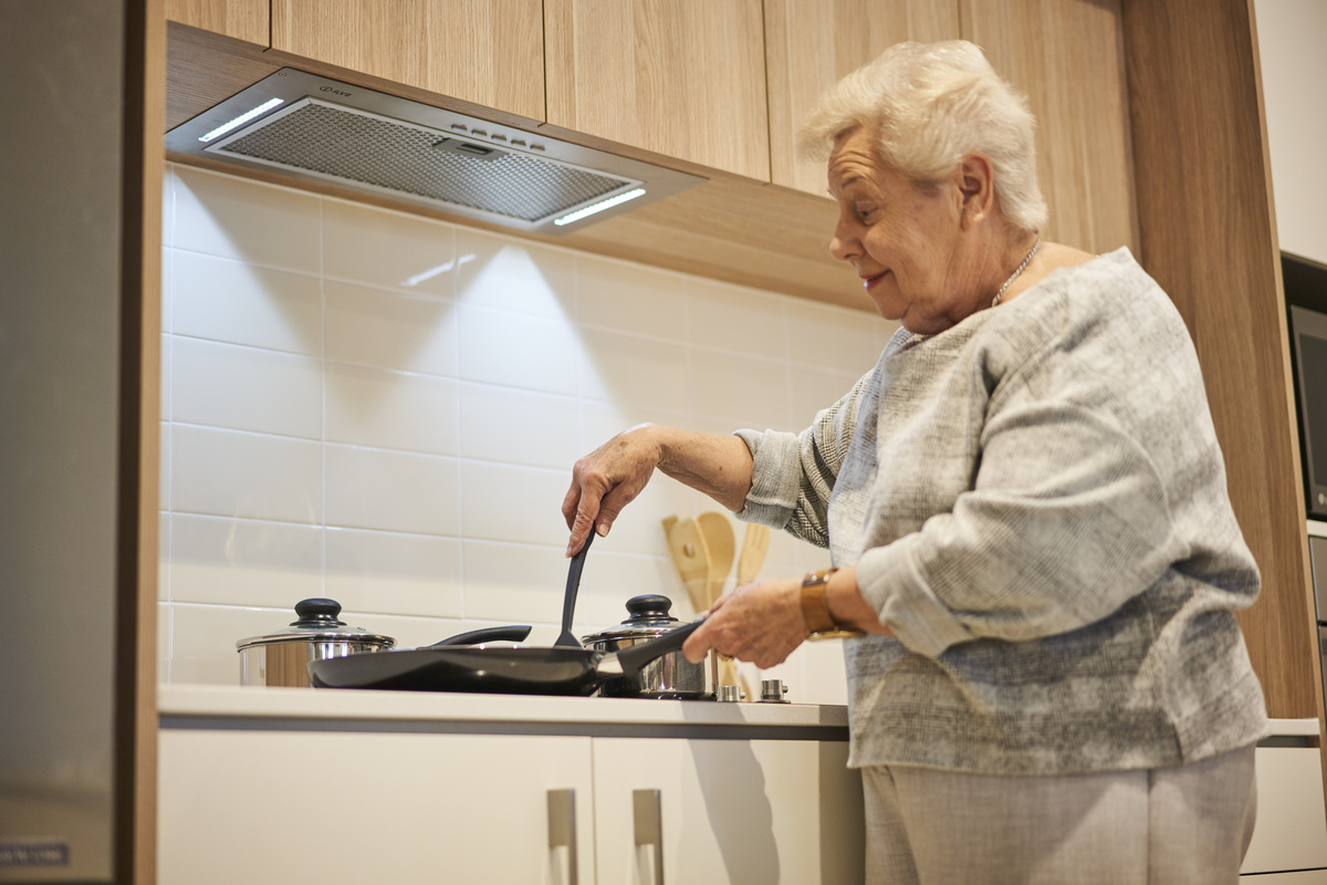 An elderly lady cooking in her kitchen in her retirement apartment