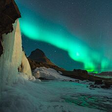 The beautiful hazy green lights of the Aurora Borealis in an icy landscape is one of the many stunning places awaiting the solo traveller in Iceland.