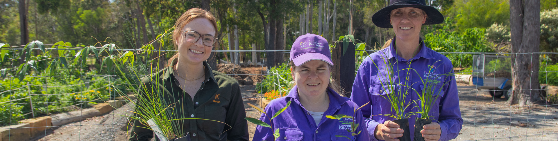 Three women holding plants and smiling at the camera