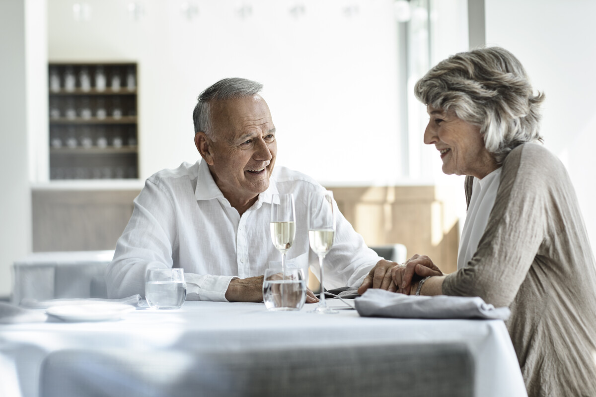 An elderly couple sitting at a restaurant table together, holding hands and smiling